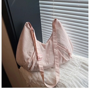 Close-up of pink crescent nylon crossbody bag with adjustable strap on white lace