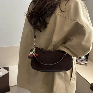 Dark brown suede underarm shoulder bag with cherry charm shown on a trench coat model
