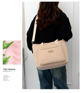 Detailed view of the beige nylon tote bag showing multiple pockets and wide shoulder strap