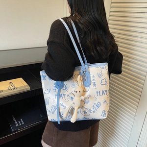 White tote bag with blue graffiti prints and rabbit charm shown in a lifestyle indoor setting