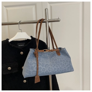 Detail of light blue leopard textured tote bag with brown straps hanging on a metal rack