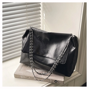 Détail d'un sac à main noir en cuir plissé avec chaîne argentée posé sur un livre