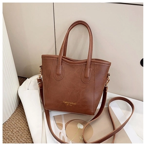 Detail of a brown textured faux leather tote bag with gold logo and shoulder strap