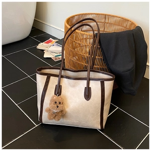 Detailed view of cream tote bag featuring brown trim and a cute teddy bear charm