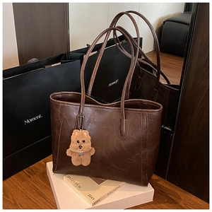 Detail of vintage brown leather tote bag texture with a cute plush bear charm accessory