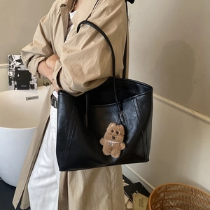 Large black matte tote bag with cute brown bear charm worn by model in a stylish interior