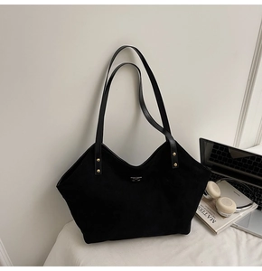 Detail of black large-capacity tote bag with golden studs on a desk with a laptop