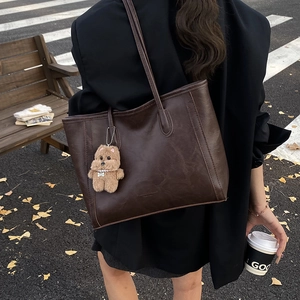 Minimalist large brown tote bag with plush dog charm in an autumn street scene setting