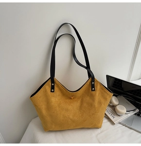 Detail of yellow quilted suede tote bag with golden lock near laptop and books