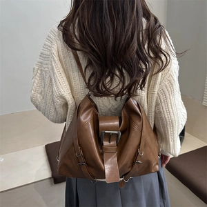 Brown vintage leather tote bag with buckle detail shown on woman in soft lighting