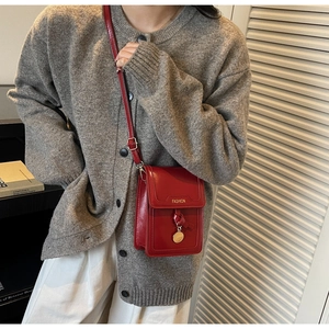 Detail of dark red crossbody bag with golden Fashion plaque and round metal pendant