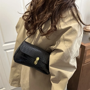 Elegant black crocodile pattern underarm bag with gold buckle on a beige trench coat