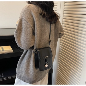 Detail view of the black glossy leather flap bag with fashion lettering and metal charm