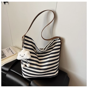 Close-up of striped canvas tote bag with brown leather strap and plush cloud charm