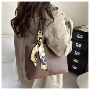 Detail of dark brown leather tote bag with a decorative printed silk scarf on the handle