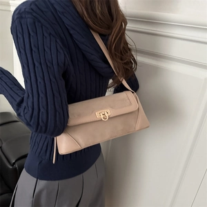 Minimalist beige suede baguette bag with gold horseshoe buckle on navy sweater model