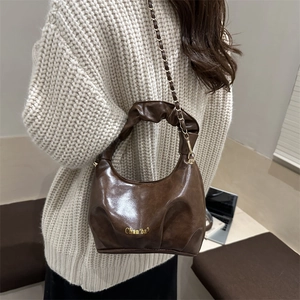 Sac nuage marron foncé à design plissé avec chaîne dorée porté par un mannequin