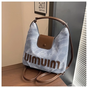 Detailansicht der hellblauen Denimtasche mit brauner Buchstabenstickerei und Ledergriff