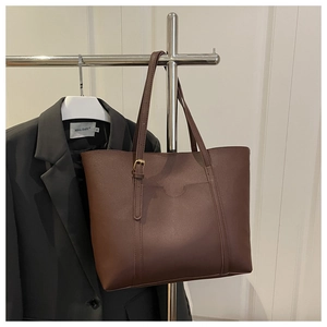 Détail d'un cabas en cuir marron foncé avec poche et boucles sur une veste de costume