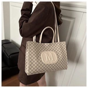Detail of elegant tote bag with M-pattern monogram print and embossed leather logo patch