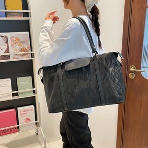 Large black travel tote bag with pleated texture and shoulder strap shown on model