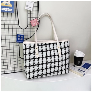Detalle de bolso tote de tweed blanco y negro con asa de cuero y remaches metálicos en mesa