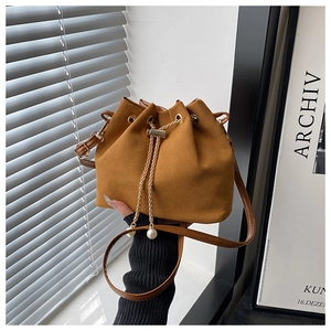 Détail d'un sac seau en daim fauve avec chaîne de serrage et breloques en perles blanches