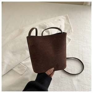Close-up of brown suede bucket bag with leather strap on soft textured background
