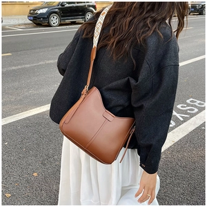 Brown leather crossbody bag with wide ethnic pattern shoulder strap shown on model outdoors