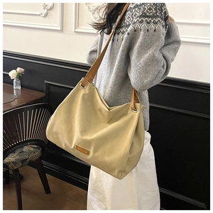 Detail of a large beige tote bag with brown leather straps shown on a model's shoulder