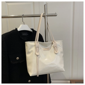Detail view of cream patent leather tote bag showing glossy texture and metal logo plate