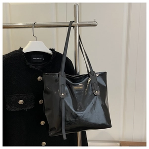 Detail of glossy black leather tote bag with gold logo badge on a silver hanger