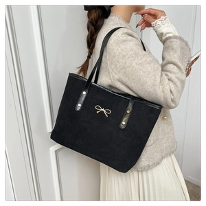 Detail of black suede tote bag featuring a gold metal bow charm and slim shoulder strap