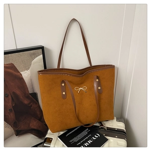Detail of golden bow ornament on large brown suede tote bag with leather straps