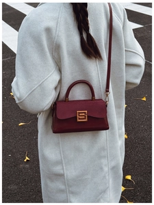 Detail of burgundy leather shoulder bag with gold square buckle worn over a grey coat
