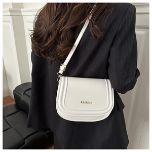 Detail of white saddle bag with golden FASHION logo over a striped blazer