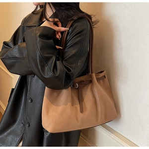 Gros plan d'un cabas en daim marron avec lanières en cuir porté avec un manteau noir