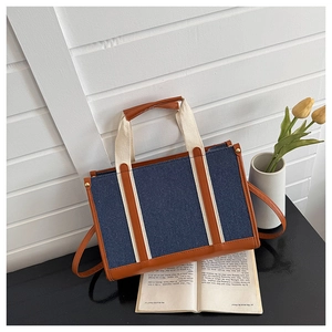 Detailansicht der marineblauen Jeans-Tasche mit braunem Lederbesatz und Stoffgriffen am Tisch