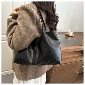 Side view of a large black matte PU leather tote bag worn by a model in a minimalist room