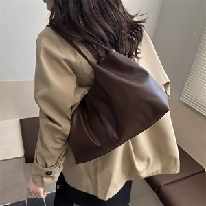 Deep brown pleated tote bag in cloud silhouette worn by model in a stylish indoor setting