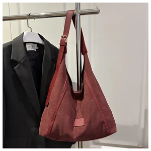 Detail of burgundy matte suede tote bag with adjustable strap on a minimalist hanger