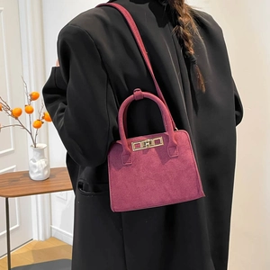 Minimalist deep pink suede handbag with gold lock shown on a black coat outfit
