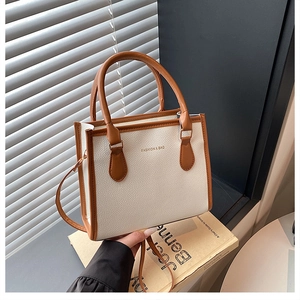 Detailed close-up of a minimalist cream tote bag with brown handles and golden lettering