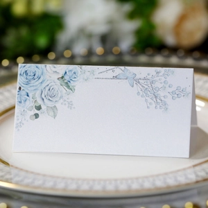 Elegant white laser-cut seat card with blue rose and butterfly on a ceramic plate