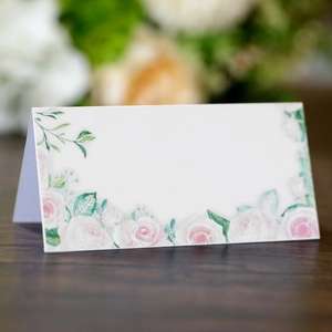 Marque-place de mariage avec roses roses et feuilles vertes sur carton blanc plié
