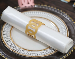 Elegant gold intertwined napkin ring on a white satin cloth over a porcelain dinner plate