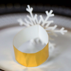 Golden paper napkin ring with white snowflake decoration on white plate for Christmas table