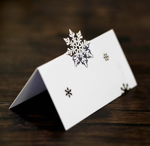 Detail of laser-cut snowflake table card in white cardstock on a wooden surface