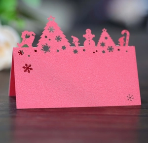 Laser cut red Christmas tree and snowman place card on dark wood table surface
