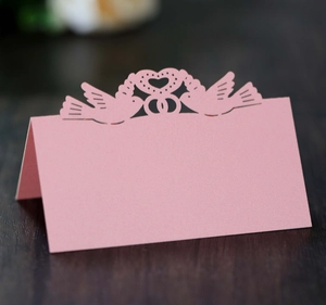 Pink laser-cut wedding place cards with heart bird design on a wooden background